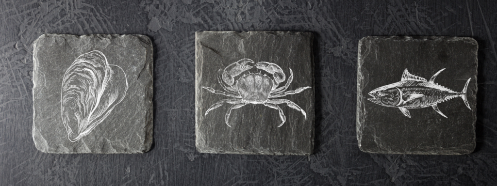 Sous-verres en ardoise gravés d’une huître, d’un crabe et d’un poisson